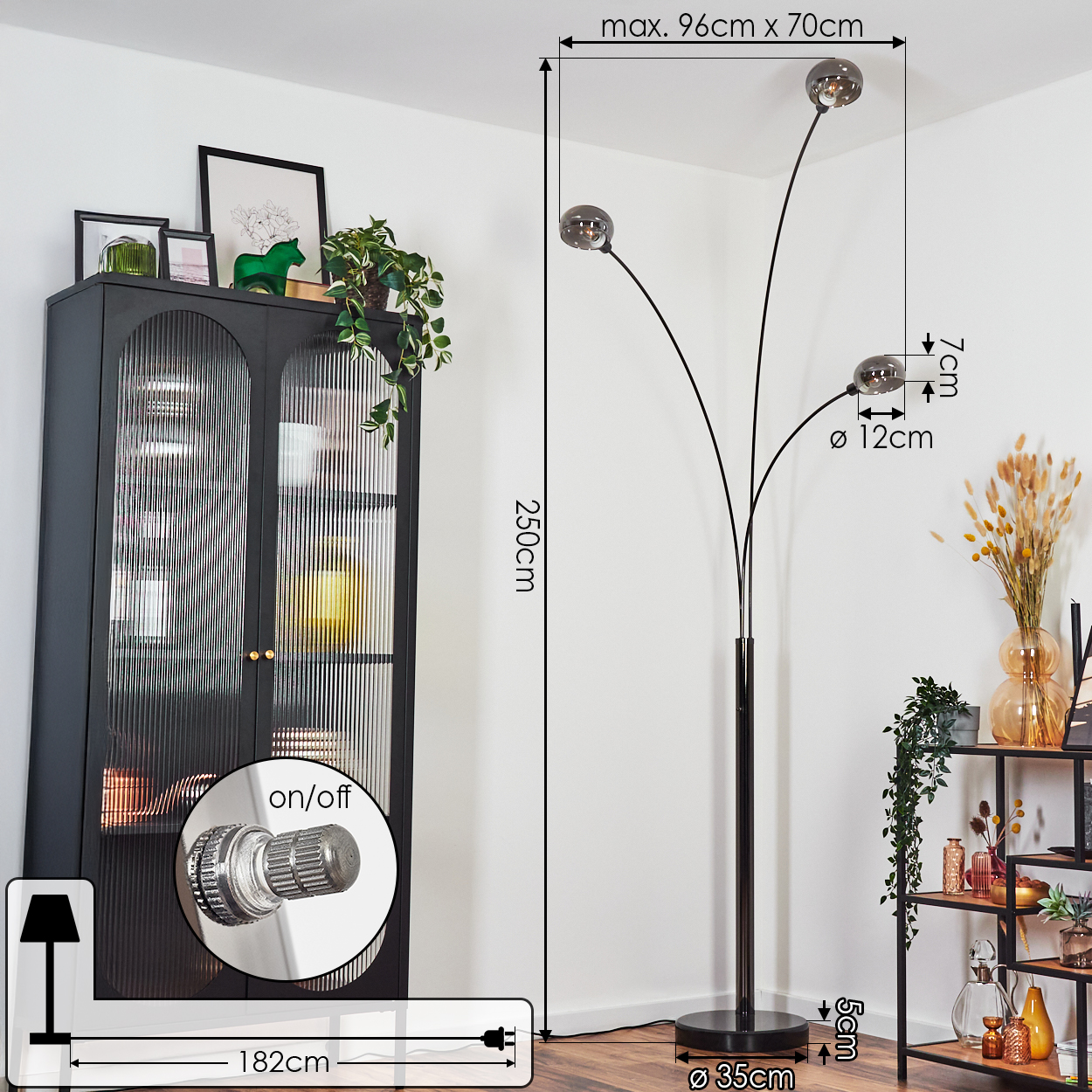 Eine moderne Stehlampe mit drei kugelförmigen Schirmen. Neben einem schwarzen Schrank mit Pflanzen und einem Regal mit Dekorationen. Abmessungen sind angegeben.
