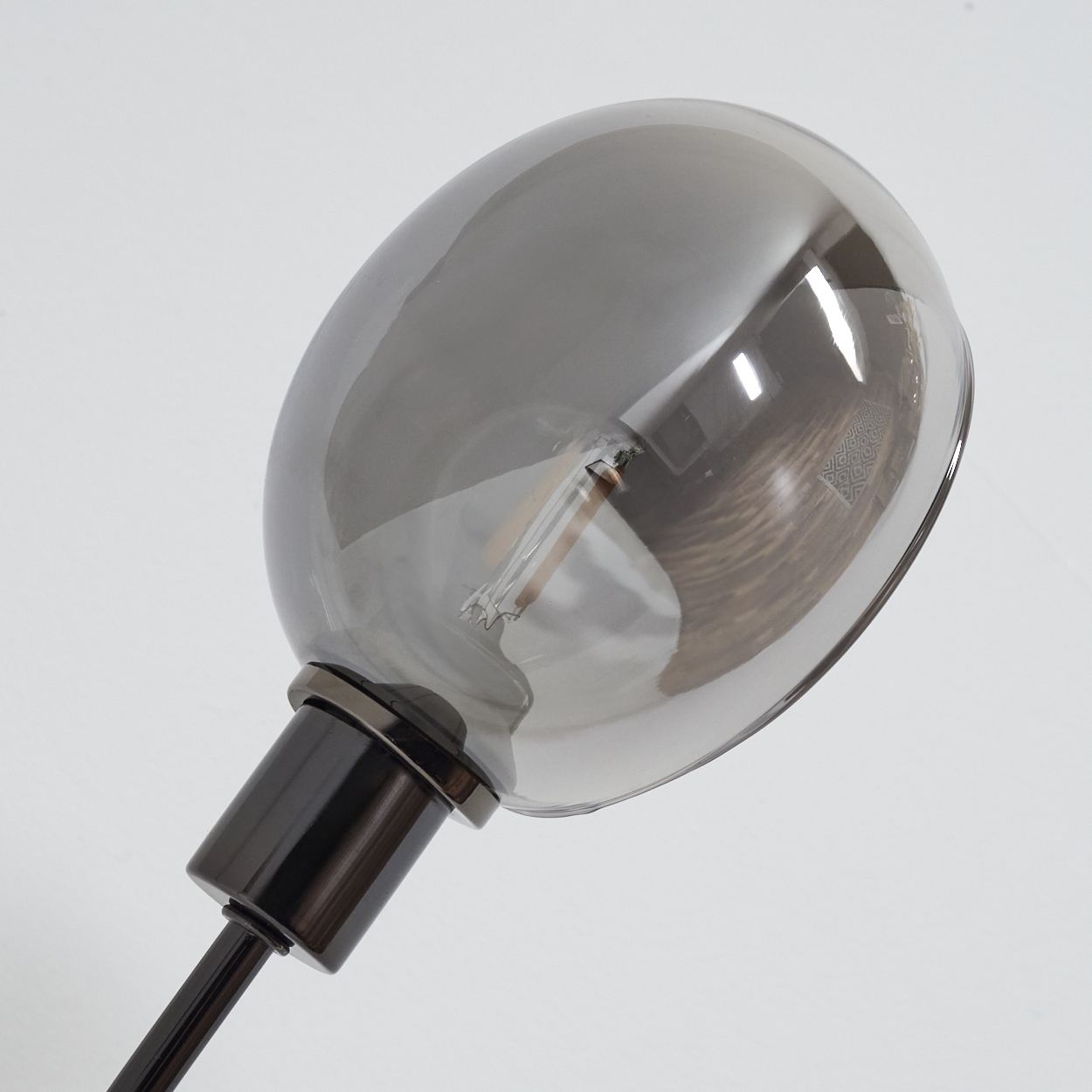 Nahaufnahme einer modernen Lampe. Sie hat eine große, graue Glaskugel und einen schwarzen Fuß und Stab, alles vor weißem Hintergrund.