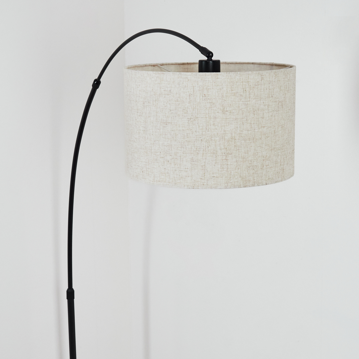 Eine moderne Stehlampe mit schwarzem gebogenem Arm und beigefarbenem Lampenschirm steht vor einer weißen Wand.