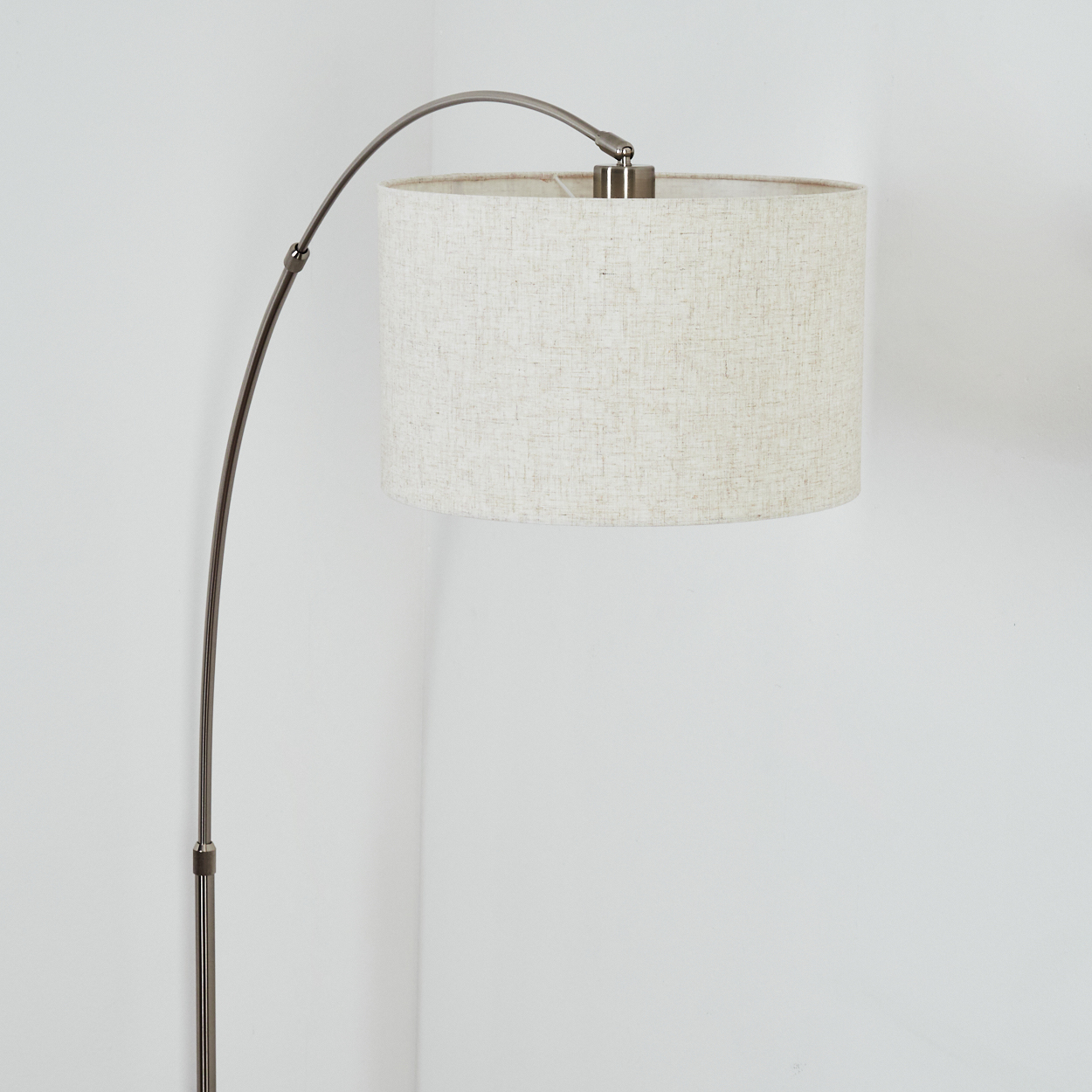 Eine moderne Bogenstehlampe mit beigem Lampenschirm. Die Lampe hat einen Metallstiel und steht vor einer weißen Wand.