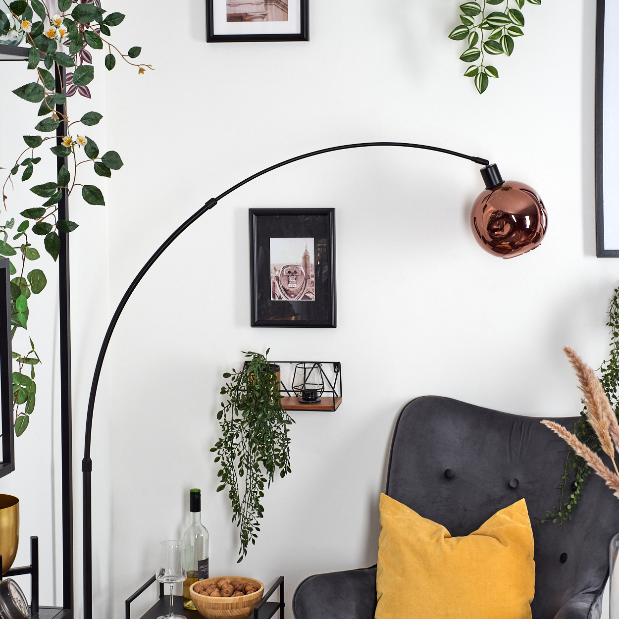 Ein Raum mit grauem Sessel, gelbem Kissen, Kupferlampe und Bildern an einer weißen Wand, dekoriert mit Pflanzen.