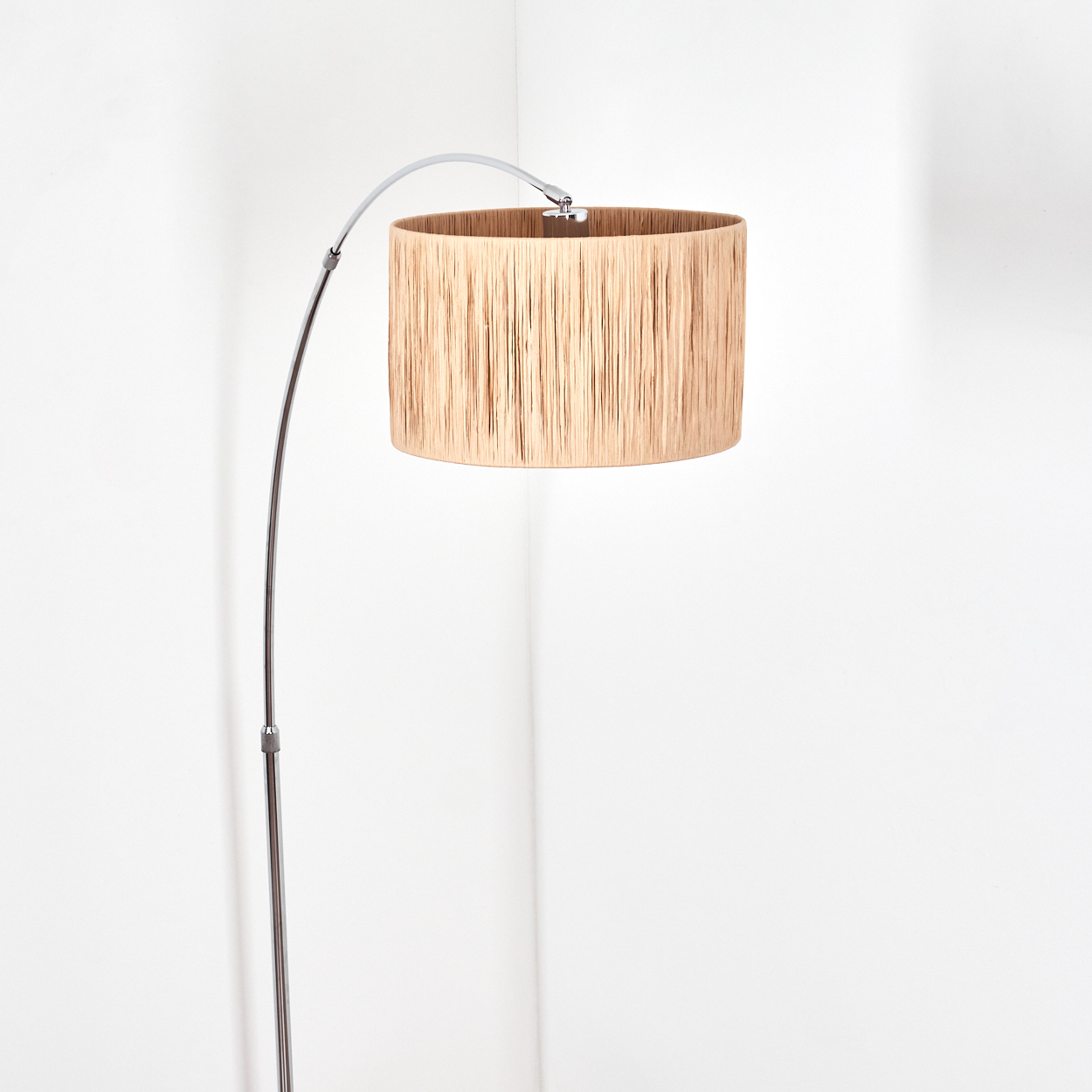 Eine moderne Stehlampe mit beigem Lampenschirm. Die Lampe hat einen gebogenen Chromarm und steht in einer weißen Ecke.