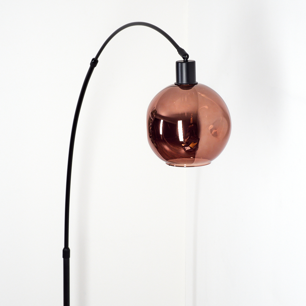 Eine moderne Stehlampe mit schwarzem, gebogenem Arm und kupferfarbenem, kugelförmigem Lampenschirm. Der Hintergrund ist weiß.