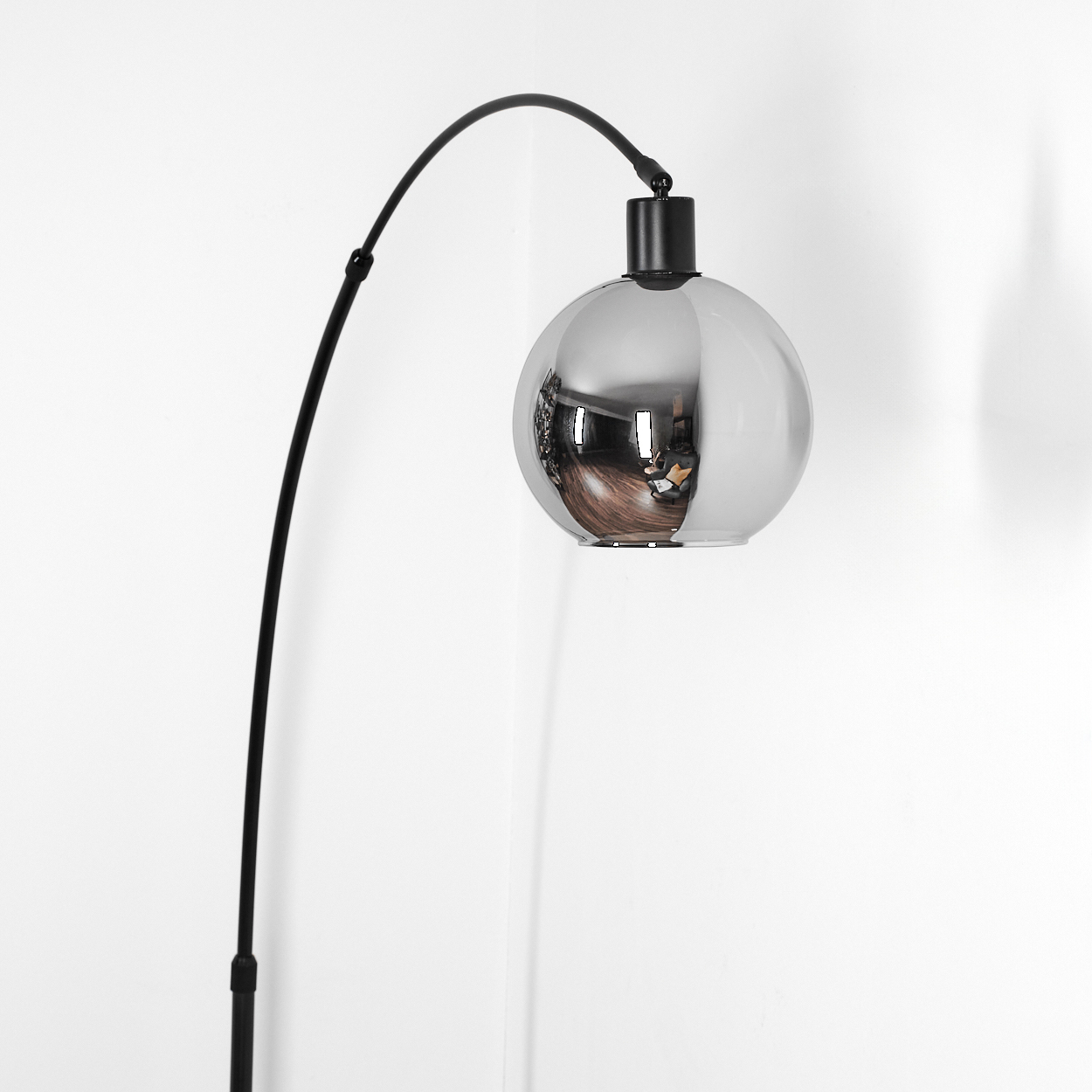 Eine moderne schwarze Bogenlampe mit verchromtem Kugelschirm. Der Schirm reflektiert den Raum. Weißer Wandhintergrund.
