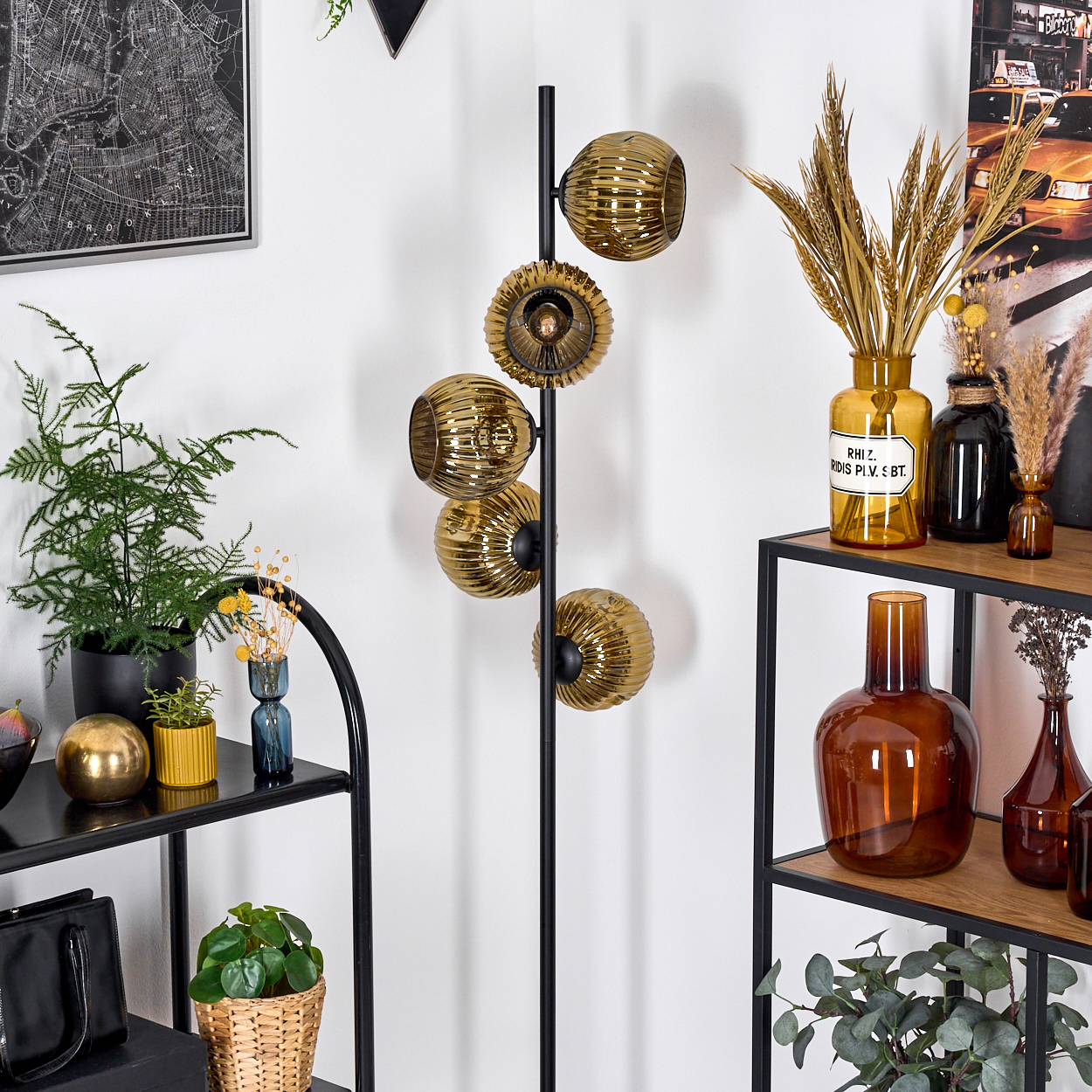Ein modernes Interieur mit einer schwarzen Lampe mit goldenen Lampenschirmen, Regalen mit Dekorationen, Pflanzen und einem Kartenbild an der Wand.