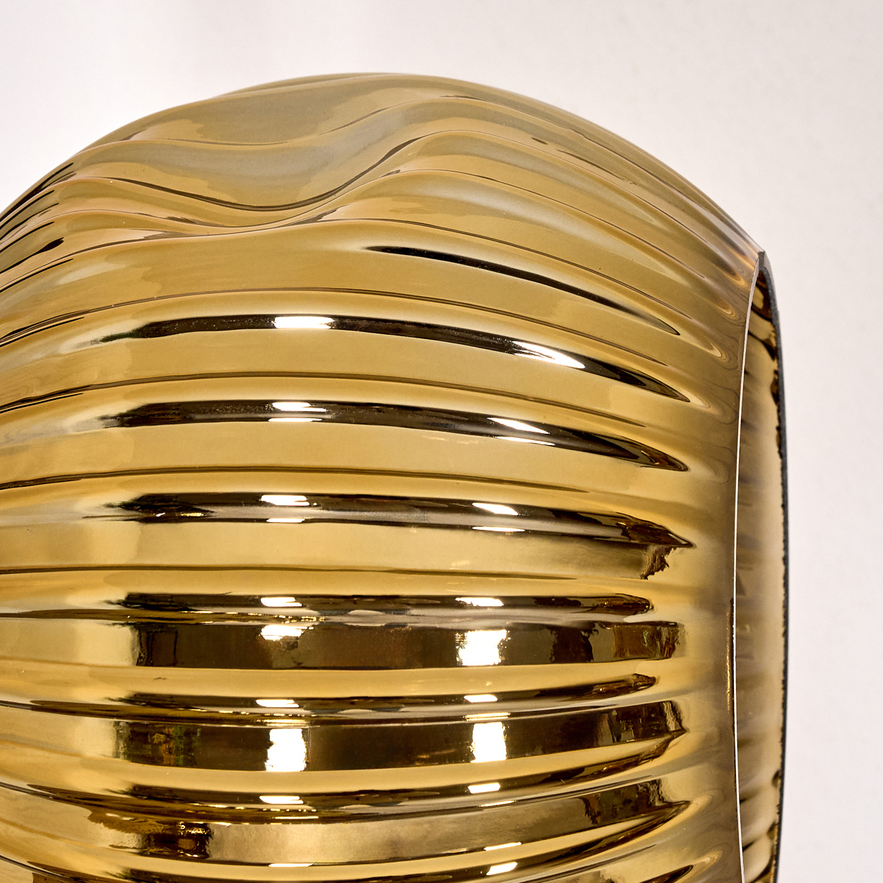 Nahaufnahme eines goldenen, zylindrischen Objekts mit horizontalen Rippen und einer gewölbten Oberseite, das Licht vor weißem Hintergrund reflektiert.