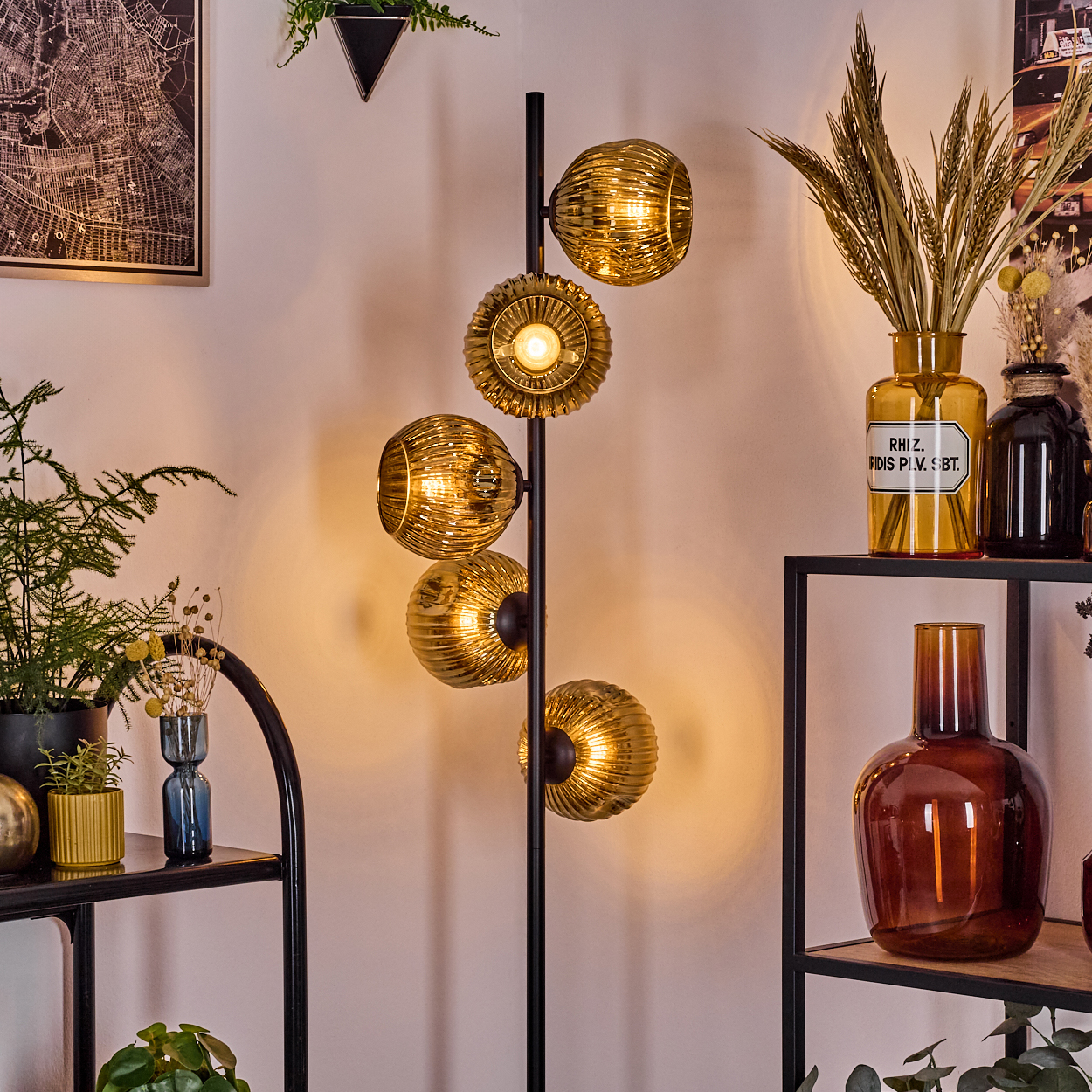 Eine moderne Stehlampe mit goldenen Kugelschirmen. Im Raum befinden sich Vasen, Pflanzen und Regale.