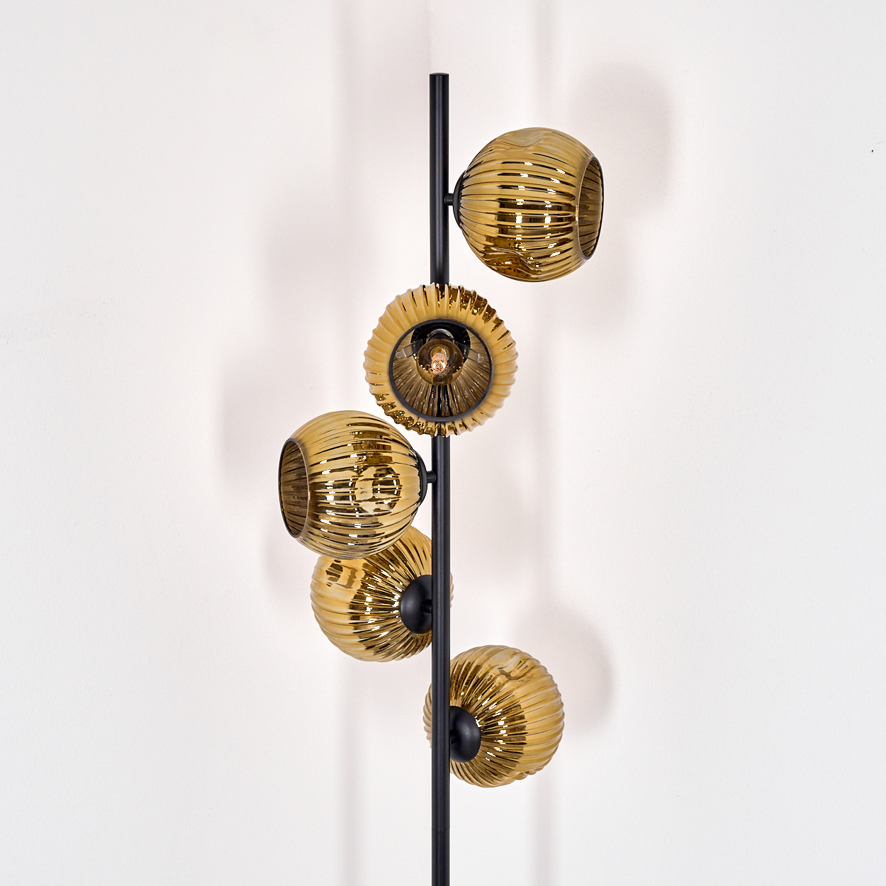 Eine moderne Lampe mit fünf goldenen Glasschirmen auf einem schwarzen Ständer vor einer weißen Wand.