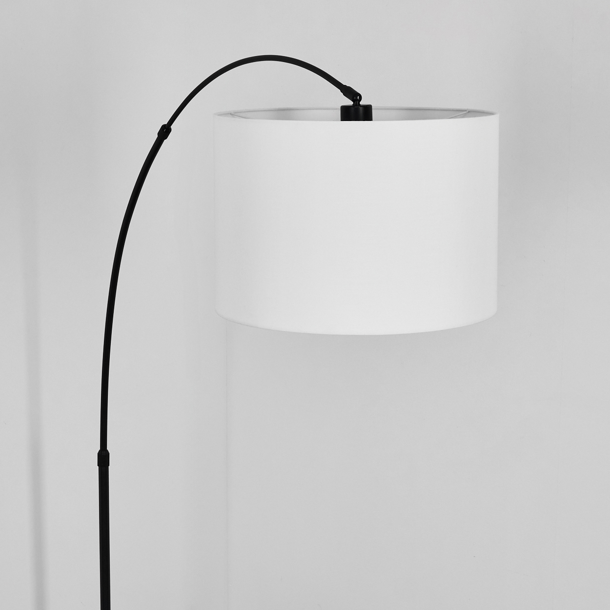 Eine moderne schwarze Stehlampe mit weißem zylindrischen Lampenschirm. Die Lampe steht vor einer schlichten weißen Wand.