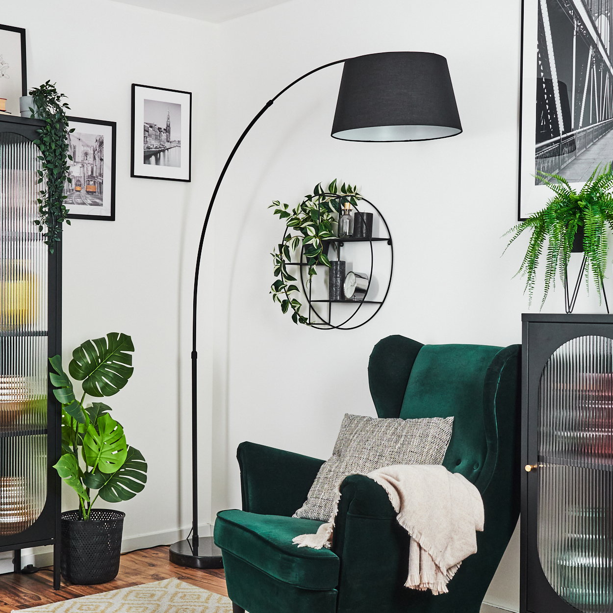 Ein grüner Sessel mit Decke und Kissen, eine schwarze Lampe, eine Pflanze, Bilder und ein Regal mit Pflanzen.