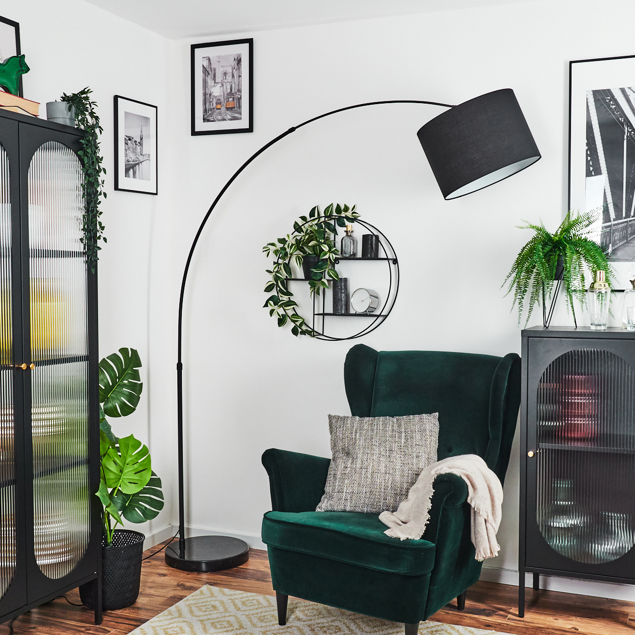 Ein grüner Sessel mit Kissen und Decke. Eine schwarze Stehlampe, Schränke und Bilder sind ebenfalls im Raum.