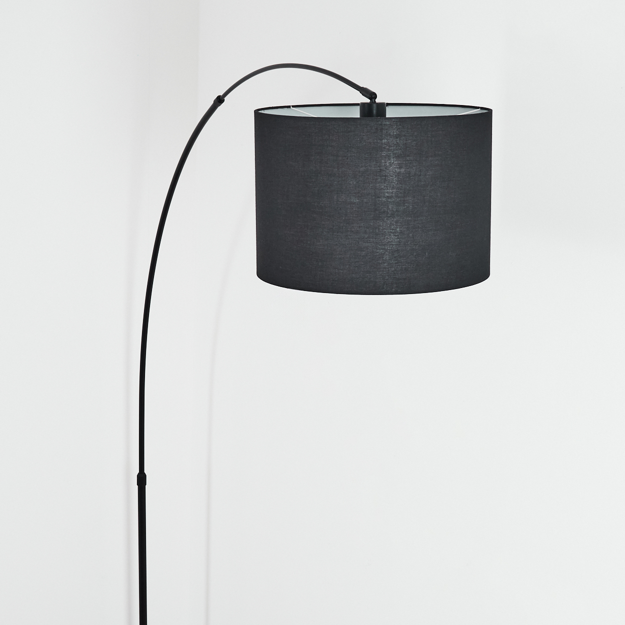 Eine moderne schwarze Bogenlampe mit zylindrischem Lampenschirm steht in einem weißen Raum. Der Schaft der Lampe ist elegant gebogen.