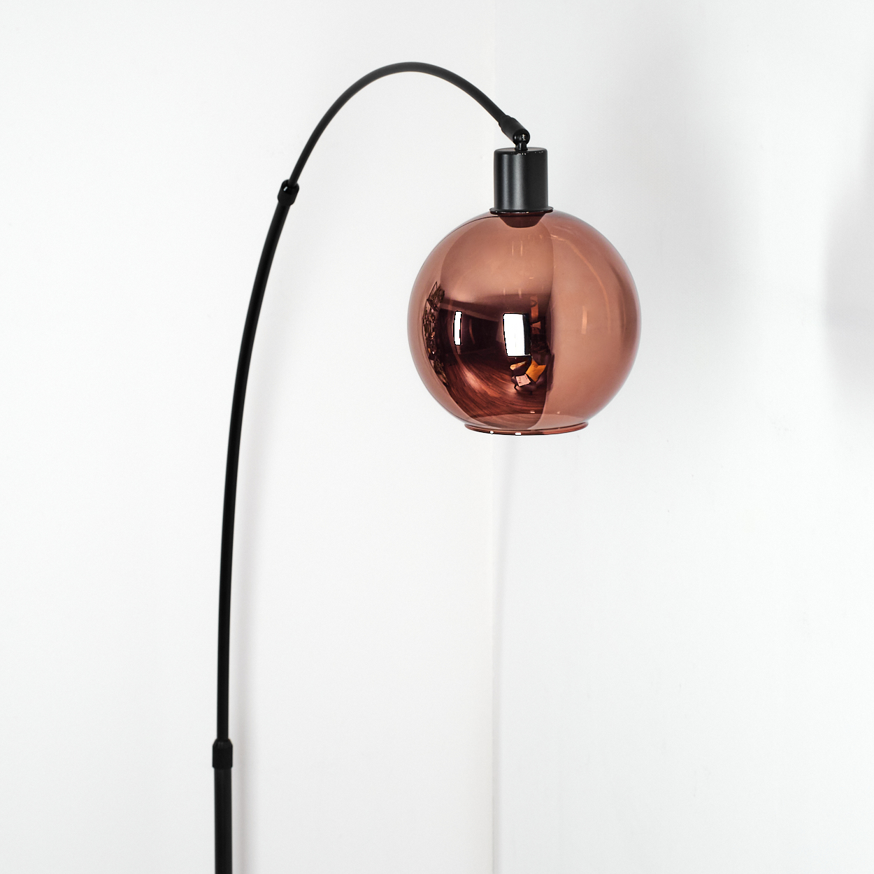 Eine moderne Stehlampe mit schwarzem, gebogenem Arm und kupferfarbenem, kugelförmigem Lampenschirm vor weißem Hintergrund.