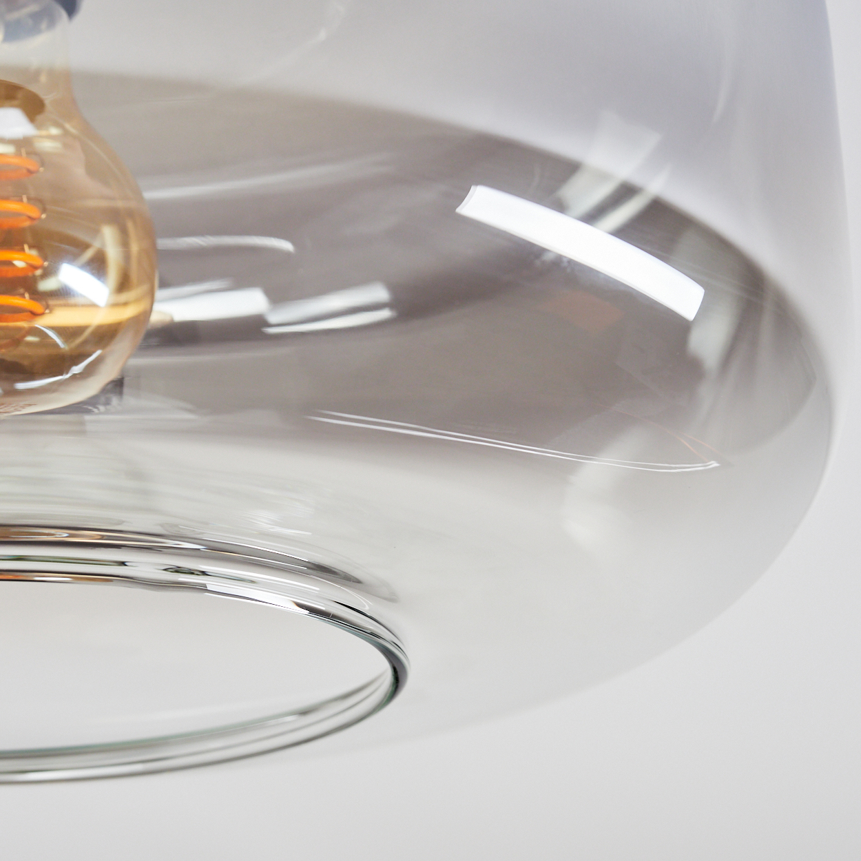 Nahaufnahme eines Glasschirms mit sichtbarer Glühbirne. Das Glas ist klar und die Glühbirne leuchtet orange.
