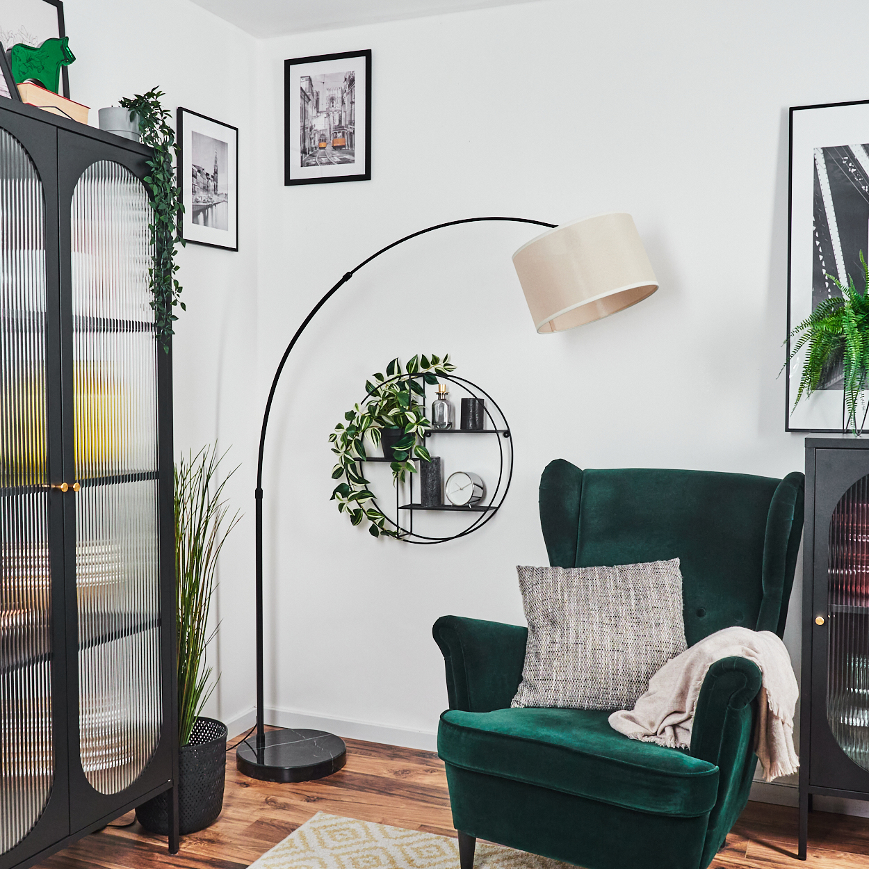 Ein grüner Sessel mit Kissen und Decke. Eine schwarze Stehlampe wölbt sich darüber. Ein schwarzer Schrank und Wandregale sind ebenfalls vorhanden.