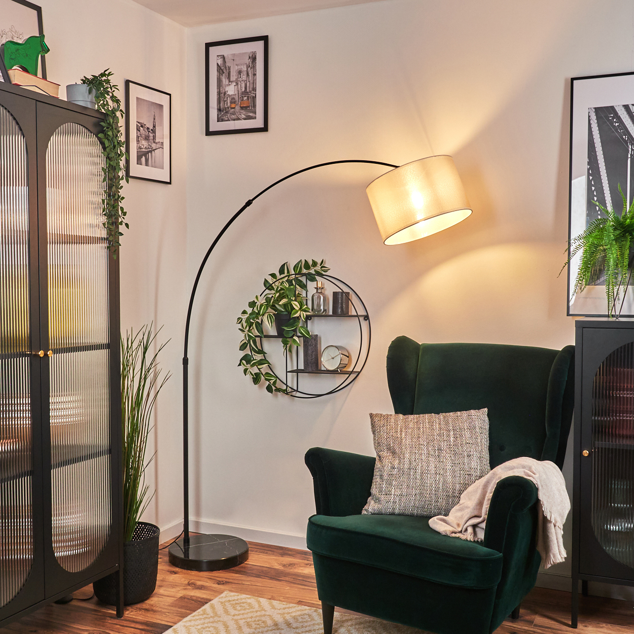 Ein grüner Sessel neben einem schwarzen Schrank und einer Stehlampe. Ein Regal mit Dekor und ein Bilderrahmen an der Wand.