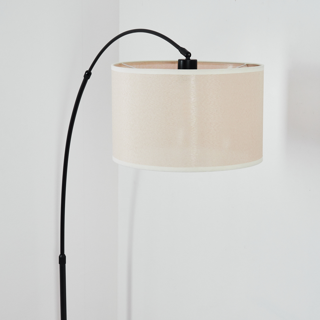 Eine moderne Stehlampe mit beigefarbenem Lampenschirm und einem schwarzen, gebogenen Arm. Der Hintergrund ist eine weiße Wand.