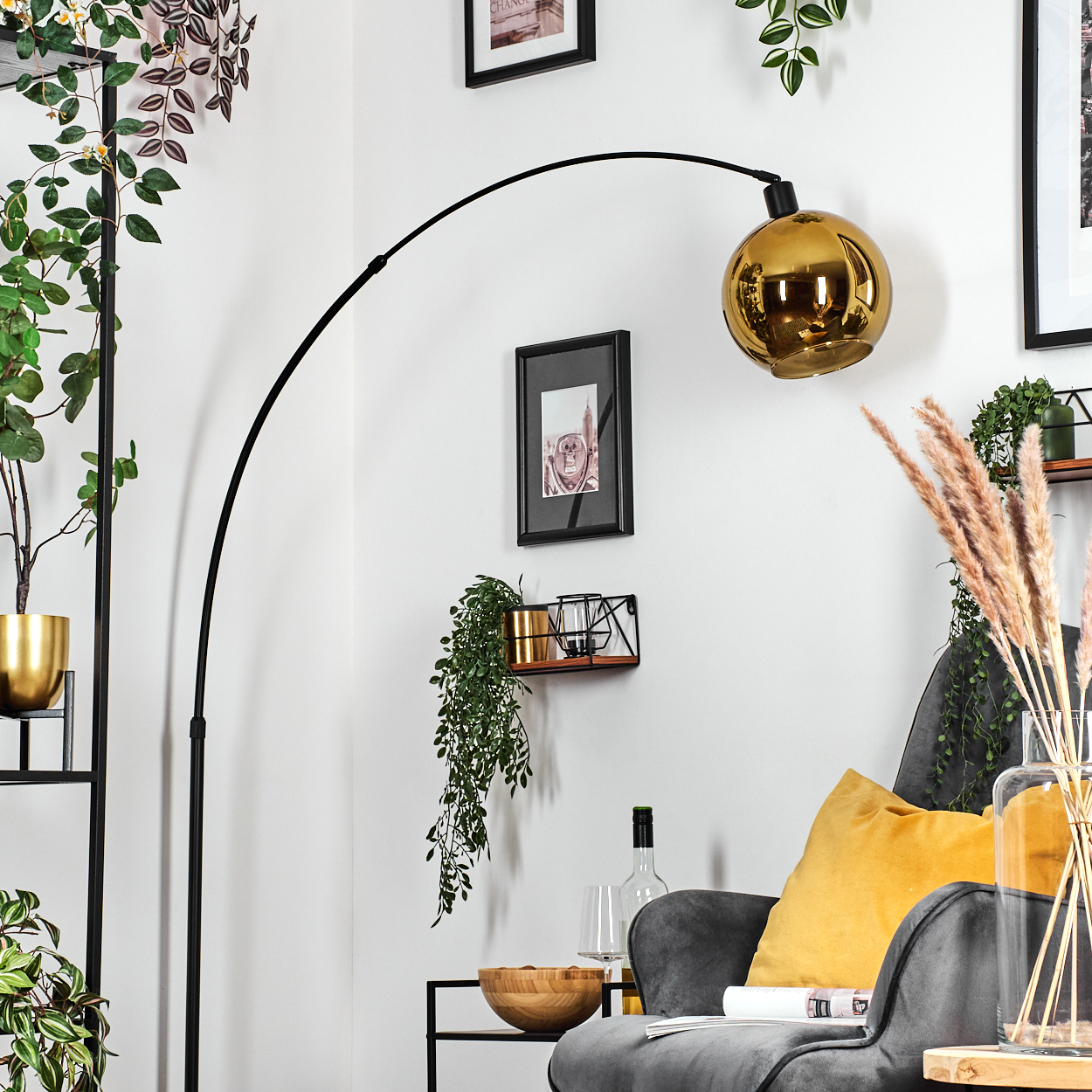 Ein modernes Wohnzimmer mit goldener Lampe, grauem Sessel und dekorativen Pflanzen. Eine Holzschale und eine Weinflasche sind ebenfalls zu sehen.