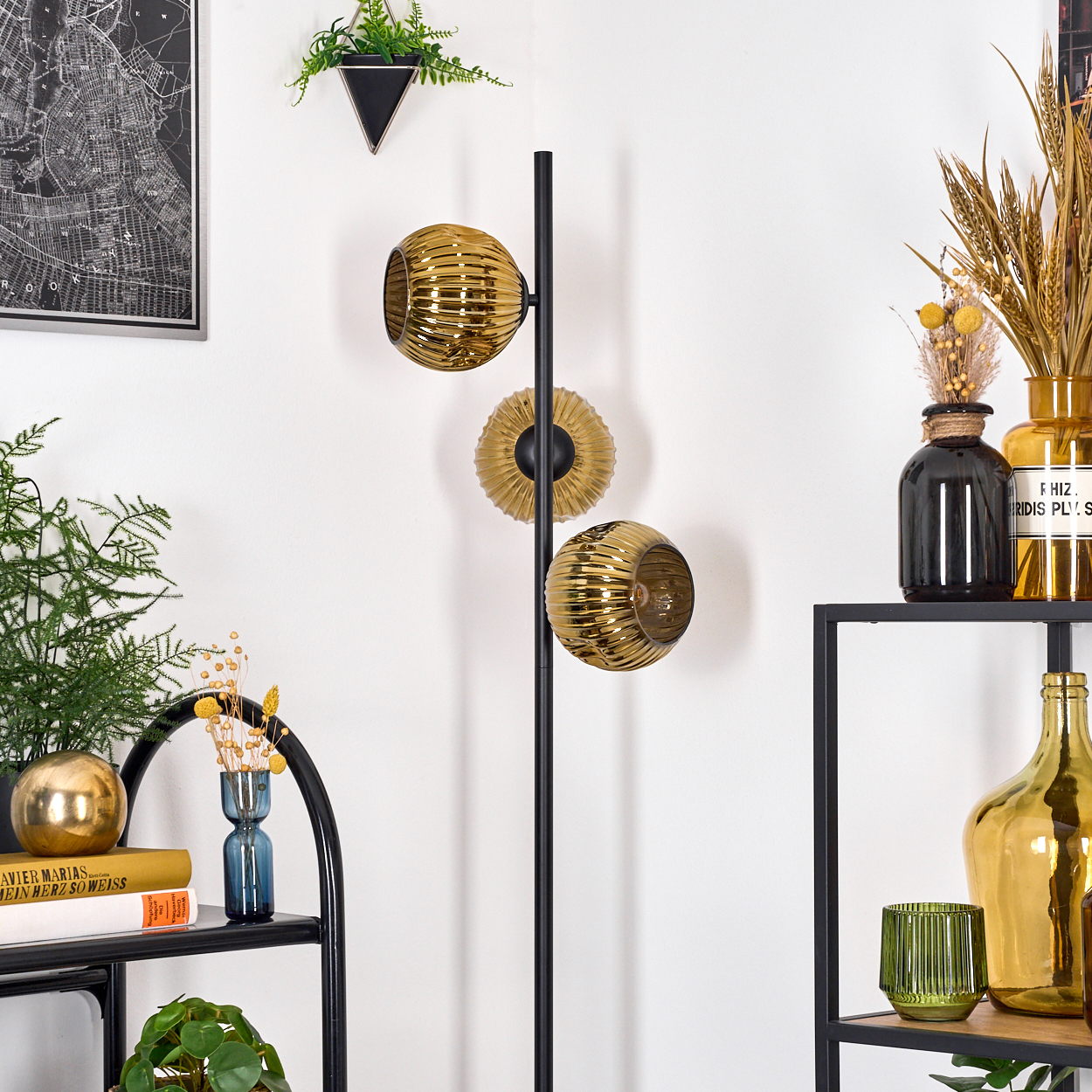 Eine moderne Raumszene mit einer schwarzen Metalllampe mit drei goldenen Glasschirmen. Regale mit Vasen und Pflanzen sind sichtbar.