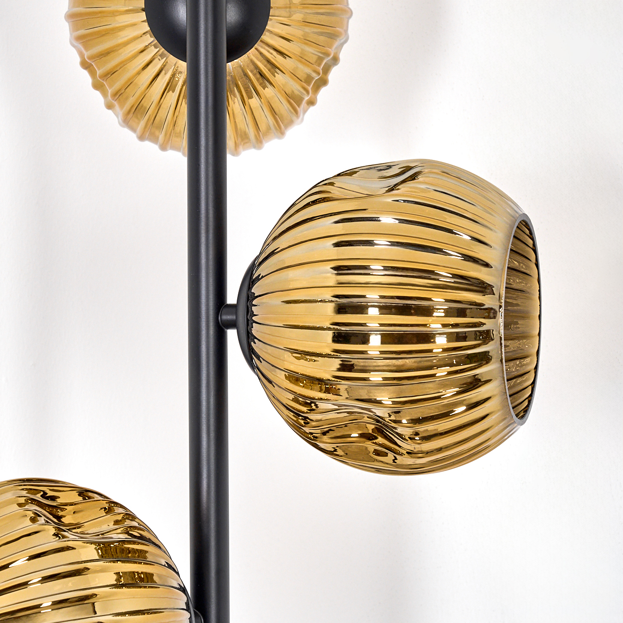 Eine moderne Lampe mit drei goldenen Glasschirmen. Die Schirme haben eine gerippte Textur, und der Rahmen ist schwarz. Weißer Hintergrund.