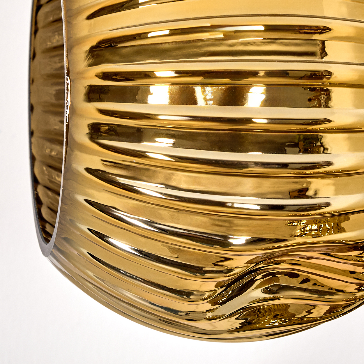 Nahaufnahme eines goldenen, gerippten, gebogenen Objekts vor weißem Hintergrund. Das Objekt ist reflektierend, mit Licht und Schatten.