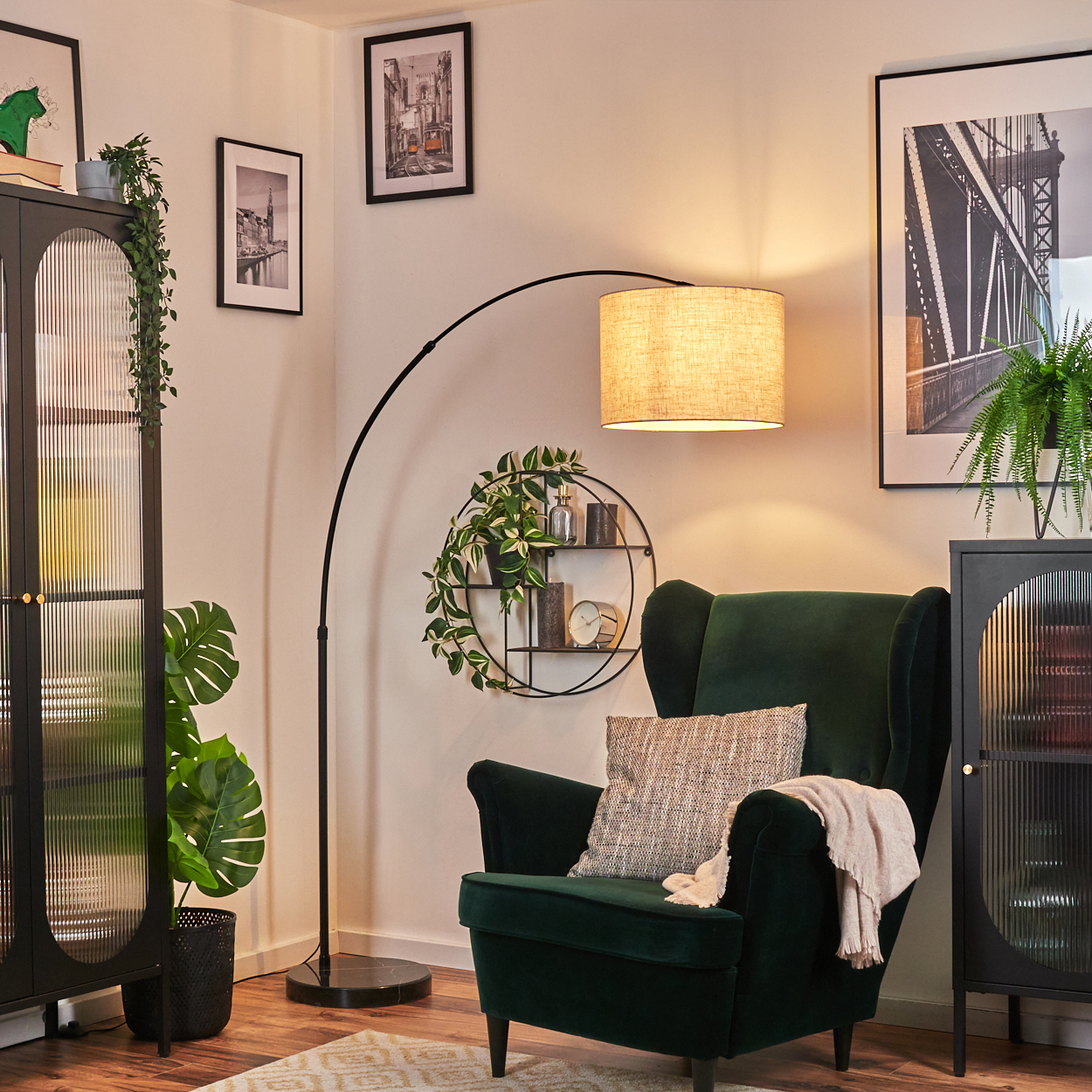 Ein dunkelgrüner Sessel mit Decke und Kissen. Eine Stehlampe beleuchtet den Stuhl. Kunstwerke und Pflanzen sind im Hintergrund.