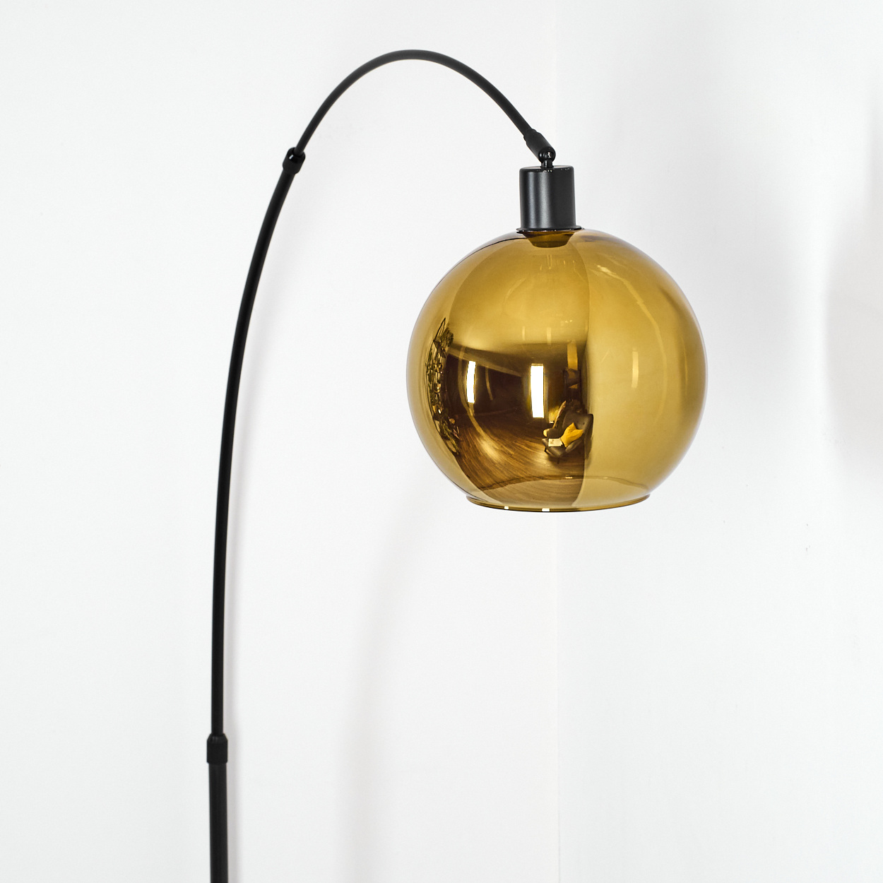 Eine moderne Lampe mit einem schwarzen, gebogenen Arm und einem goldenen Kugelschirm an einer weißen Wand.