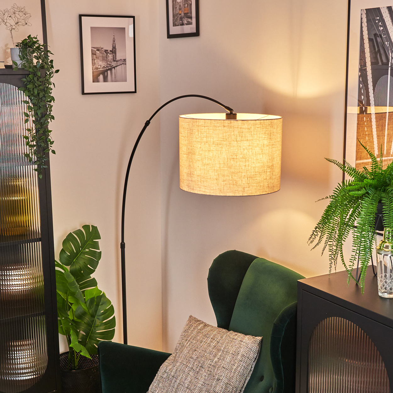 Ein Raum mit einem grünen Sessel, einer Stehlampe und Pflanzen. Kunstwerke hängen an den Wänden. Rechts befindet sich ein Schrank.
