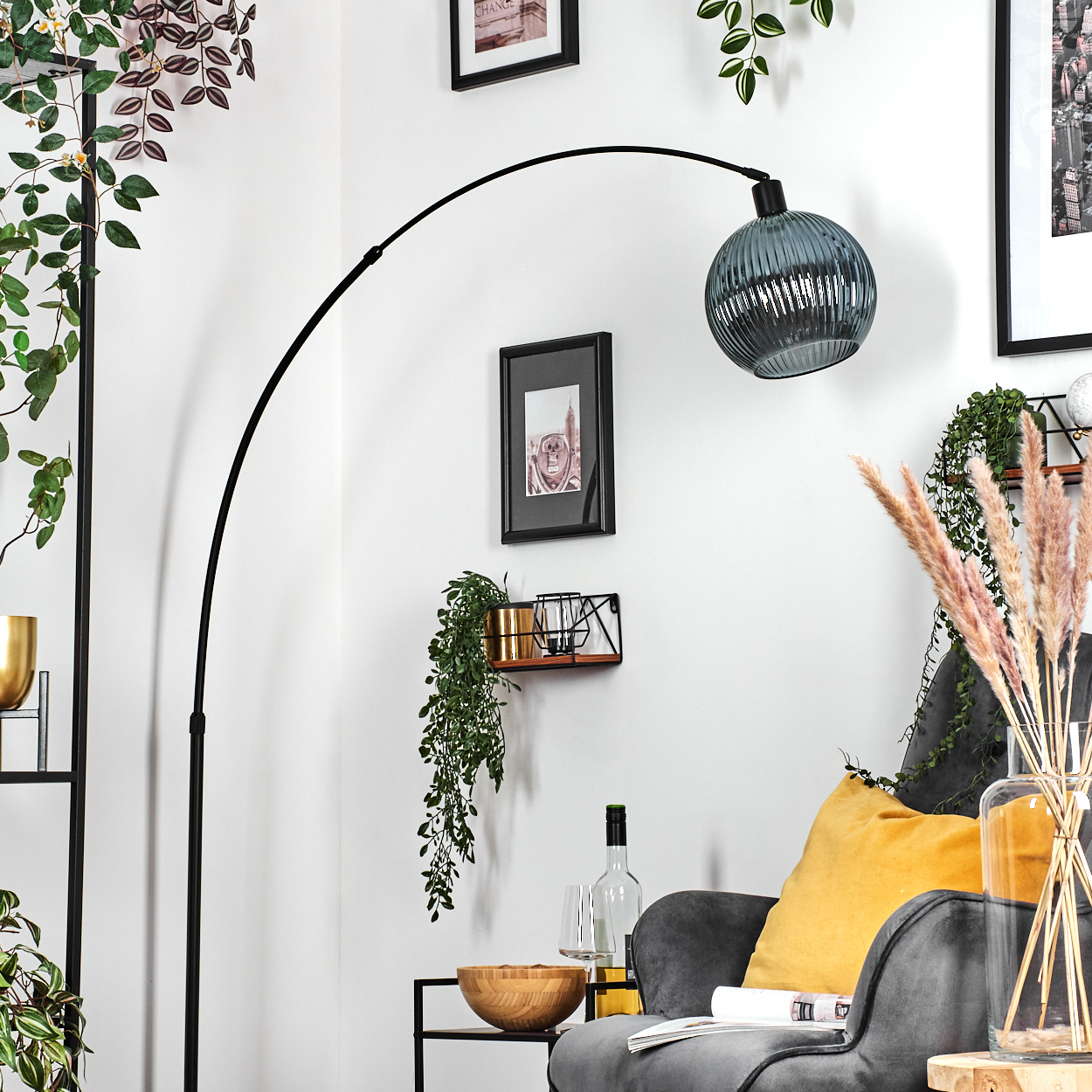 Ein modernes Wohnzimmer mit schwarzer Bogenlampe, grauem Sessel und dekorativen Elementen wie Pflanzen und gerahmten Bildern.