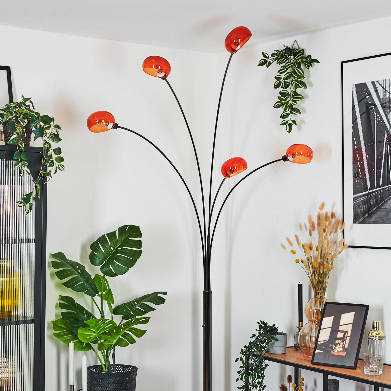 Ein modernes Wohnzimmer mit einer schwarzen Stehlampe mit orangefarbenen Kugellampen, Pflanzen, einem Bild und einem Holzregal.