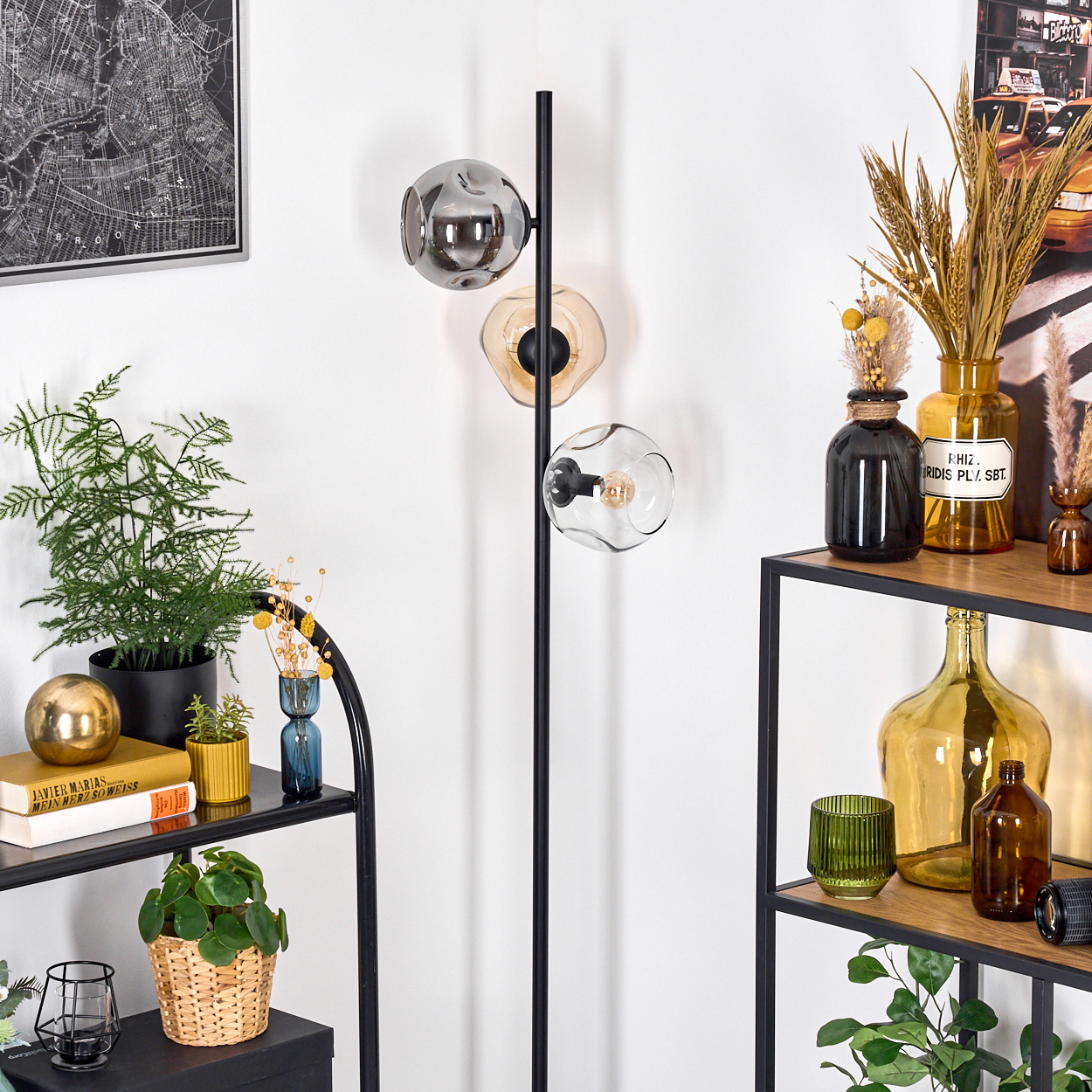 Ein Raum mit einer schwarzen Stehlampe mit drei Glaskugeln, Regalen mit Pflanzen und Vasen und einem Kartenbild.