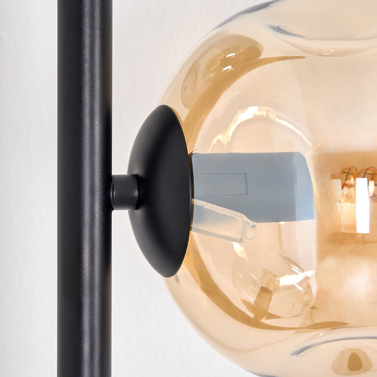 Nahaufnahme einer Lampe. Mit schwarzem Metallträger, kugelförmigem bernsteinfarbenem Glasschirm und Glühbirne. Der Hintergrund ist weiß.