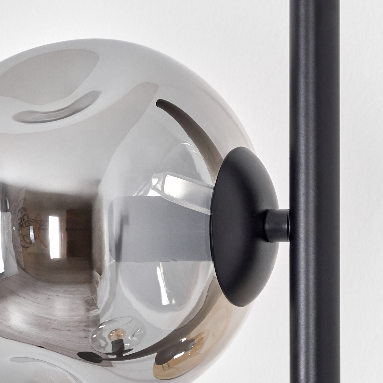 Nahaufnahme einer modernen Leuchte. Sie hat eine rauchige Glaskugel, einen schwarzen kreisförmigen Sockel und einen schwarzen Metallpfahl vor weißem Hintergrund.