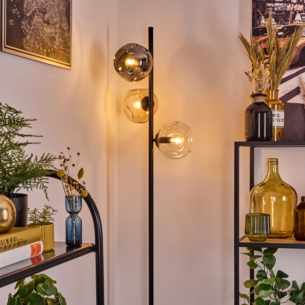 Eine moderne Lampe mit drei Glaskugeln leuchtet. Regale mit Vasen, Pflanzen und Büchern befinden sich im Hintergrund.