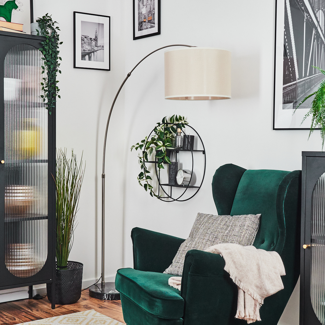 Ein grüner Sessel mit Decke und Kissen, eine Stehlampe und ein schwarzer Schrank mit Pflanzen, Bildern und einem runden Regal.