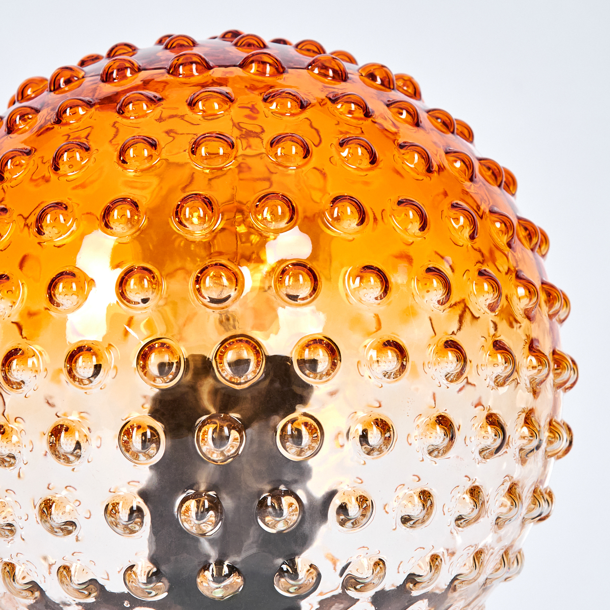 Nahaufnahme einer kugelförmigen Glaslampe mit orangefarbenen und klaren Blasen. Der Hintergrund ist weiß.
