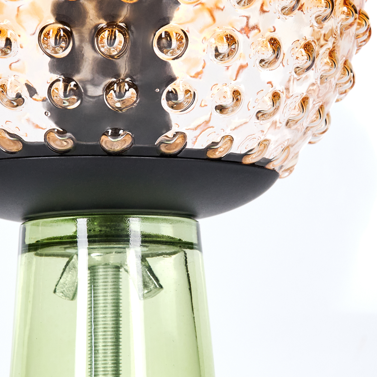 Nahaufnahme einer Lampe. Sie hat einen grünen Glassockel und einen Lampenschirm aus Glas mit Blasen. Der obere Teil ist schwarz.