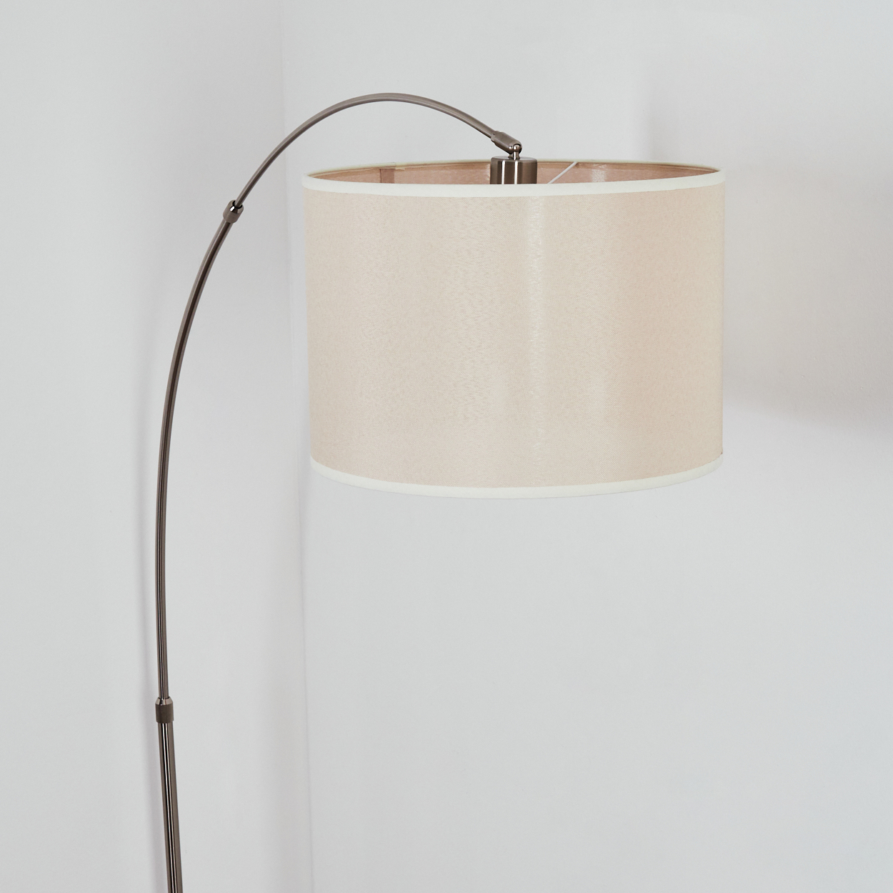Eine moderne Stehlampe mit beigem Lampenschirm. Sie hat einen gebogenen, dunklen Metallrahmen. Der Hintergrund ist eine weiße Wand.