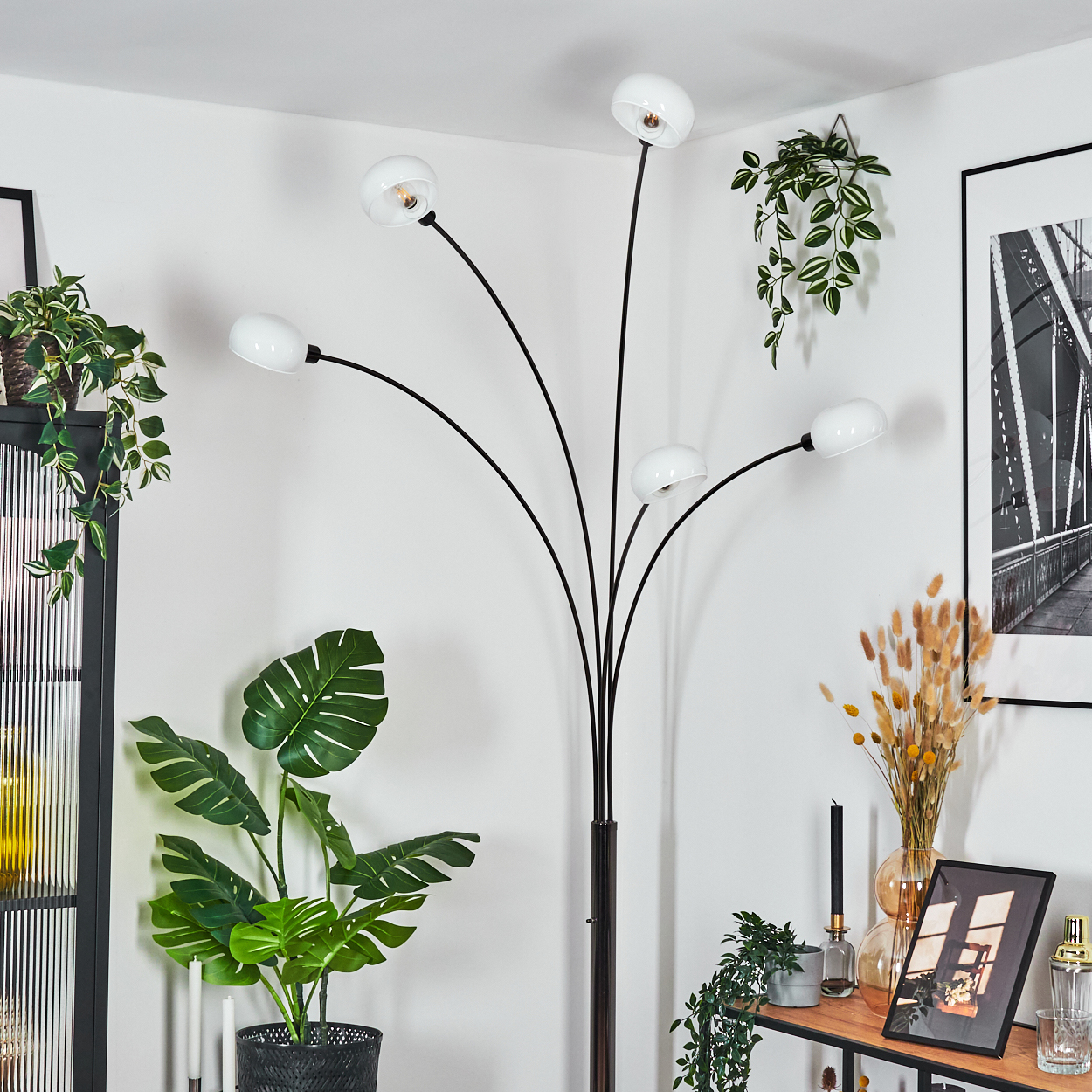 Ein modernes Zimmer mit einer schwarzen Stehlampe, Pflanzen und einem gerahmten Brückenfoto. Die Lampe hat fünf weiße Kugellampen.