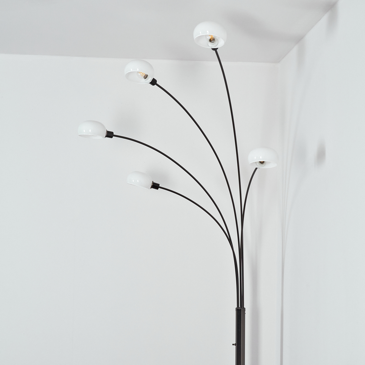 Eine moderne Stehlampe mit fünf weißen Lampenschirmen. Schwarze, gebogene Arme erstrecken sich von einem zentralen schwarzen Pfosten.