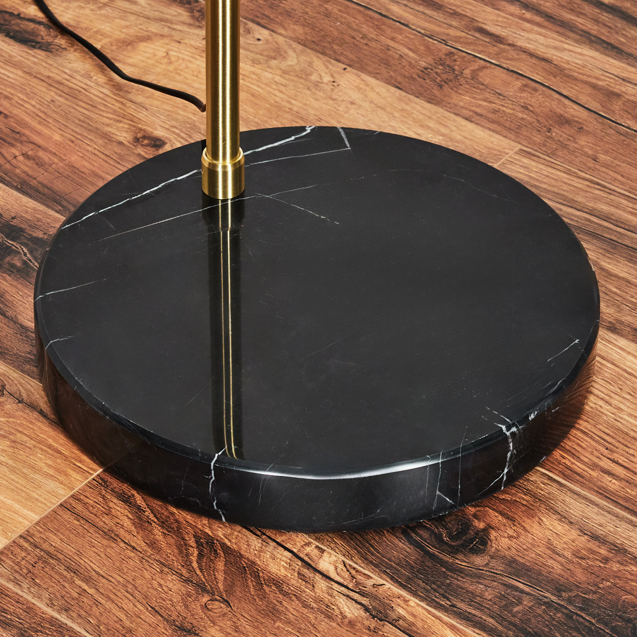 Ein schwarzer Marmorlampensockel mit weißen Adern. Ein goldener Lampenständer ragt aus dem Sockel, ein schwarzes Kabel ist sichtbar.
