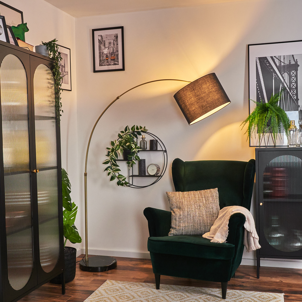 Ein dunkelgrüner Sessel mit Kissen und Decke. Eine schwarze Lampe, ein Regal mit Deko und ein schwarzer Schrank sind ebenfalls vorhanden.