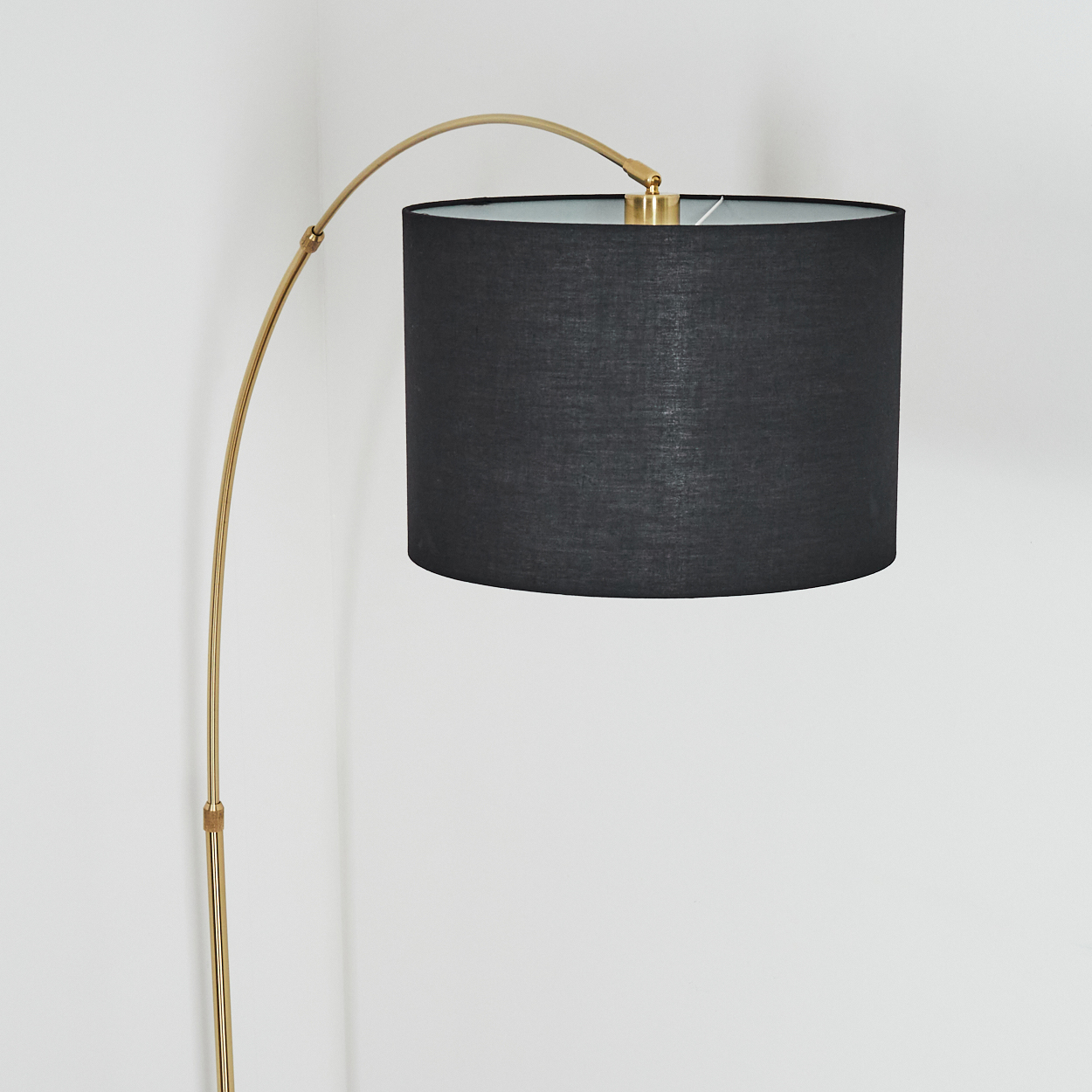 Eine moderne Stehlampe mit goldenem Stiel und schwarzem Lampenschirm vor einer weißen Wand.