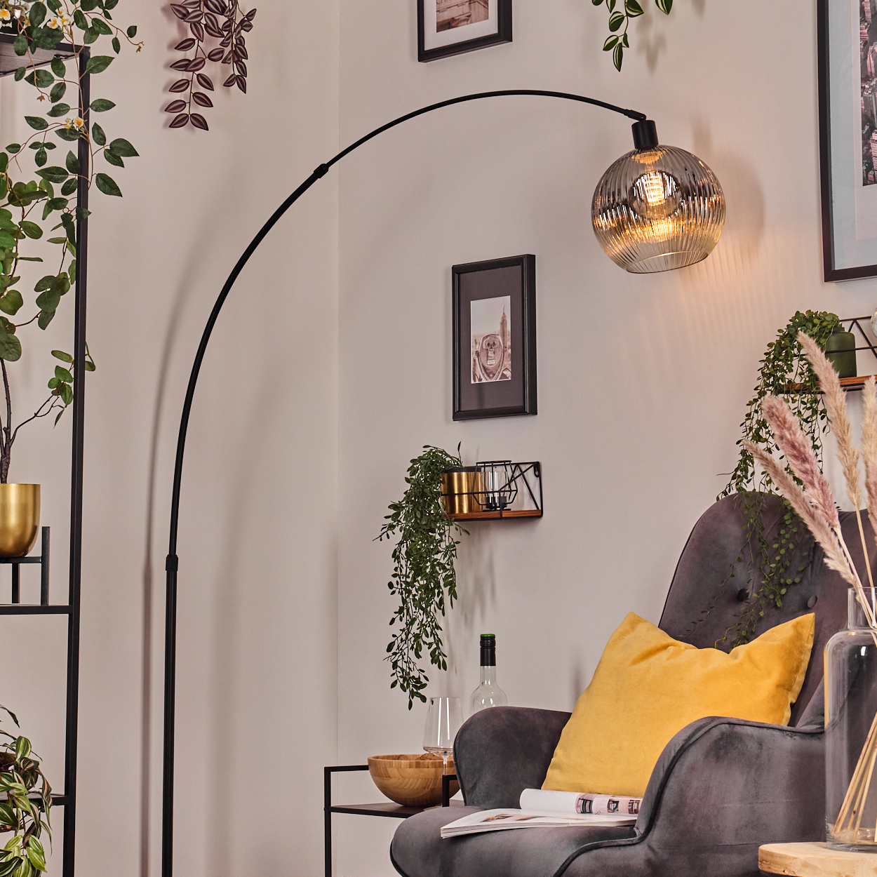 Modernes Wohnzimmer mit grauem Sessel, gelbem Kissen, gebogener Stehlampe und Zierpflanzen. Eine Glaslampe hängt oben.