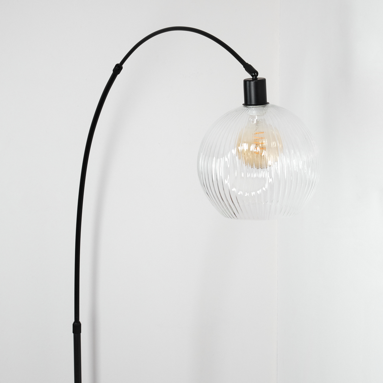 Eine moderne schwarze Stehlampe mit einem klaren, gerippten Glaskugel-Schirm. Die Glühbirne ist sichtbar, vor weißem Hintergrund.