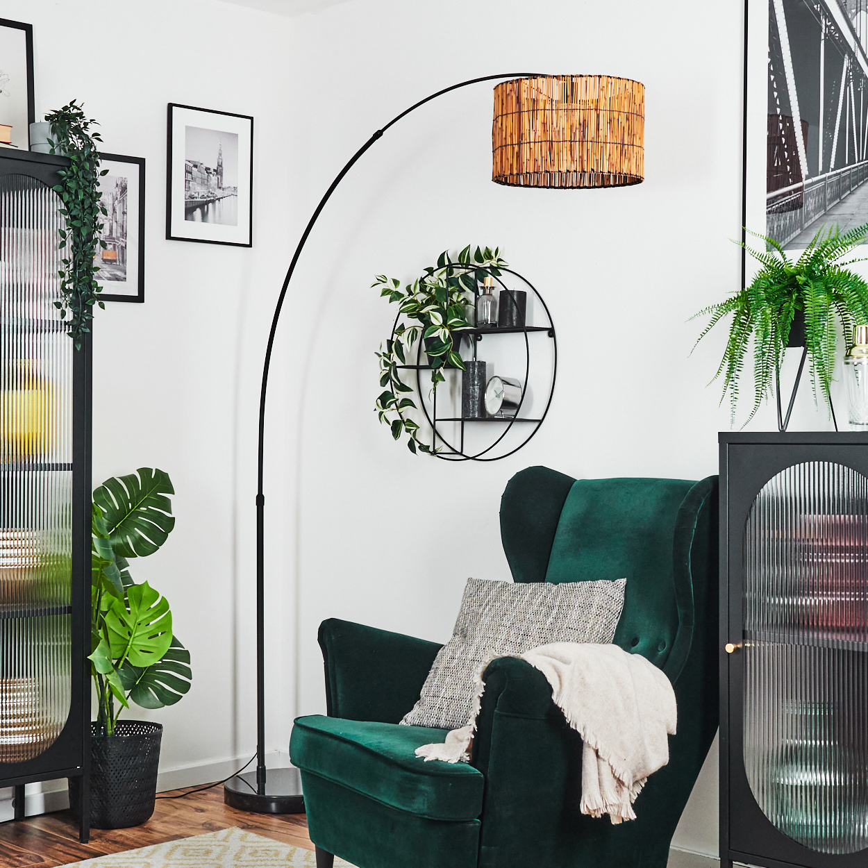 Ein grüner Sessel mit Kissen und Decke. Eine Stehlampe mit gewebtem Lampenschirm. Pflanzen und gerahmte Bilder sind sichtbar.
