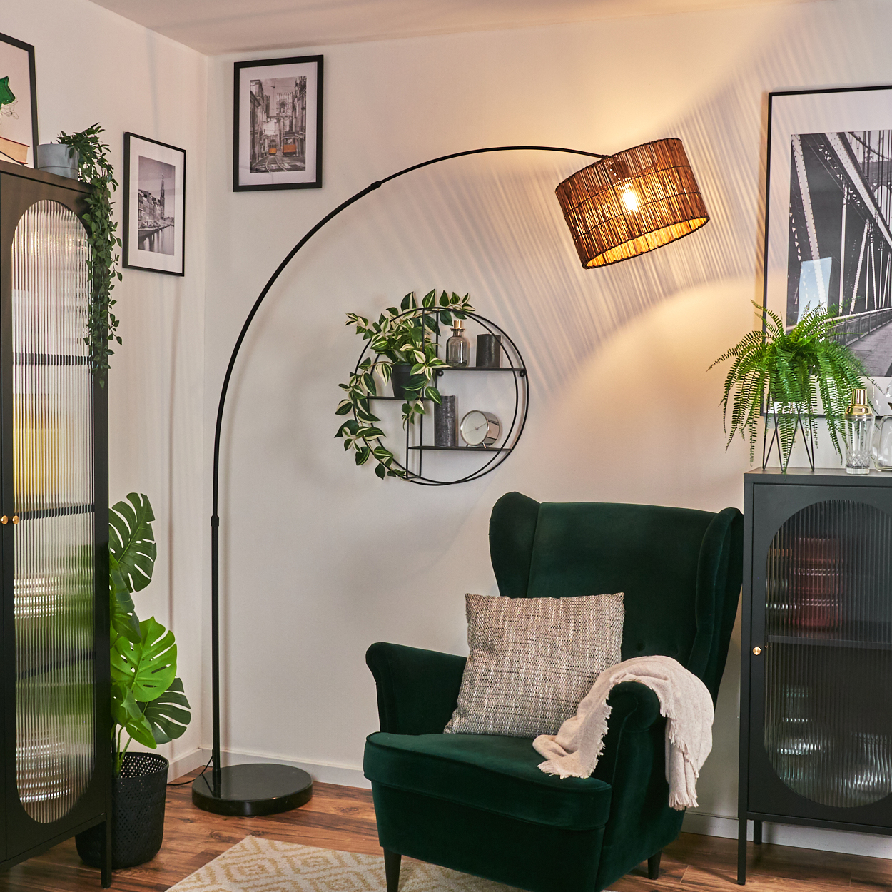 Ein grüner Sessel mit Kissen und Decke, eine Stehlampe, ein Beistelltisch mit Pflanzen und Bilder an der Wand.