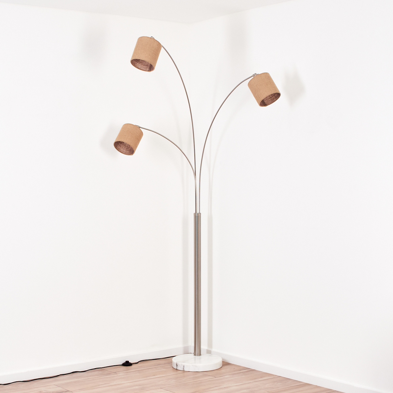 Eine Stehlampe mit drei Lampenschirmen. Die Lampe hat ein silbernes Metallgestell mit Marmorsockel. Beige Lampenschirme zeigen in verschiedene Richtungen.
