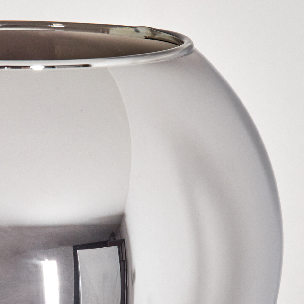 Nahaufnahme einer klaren Glasvase. Die Vase reflektiert den Raum, einschließlich einer weißen Lichtquelle und der Decke. Die Vase ist im Fokus.