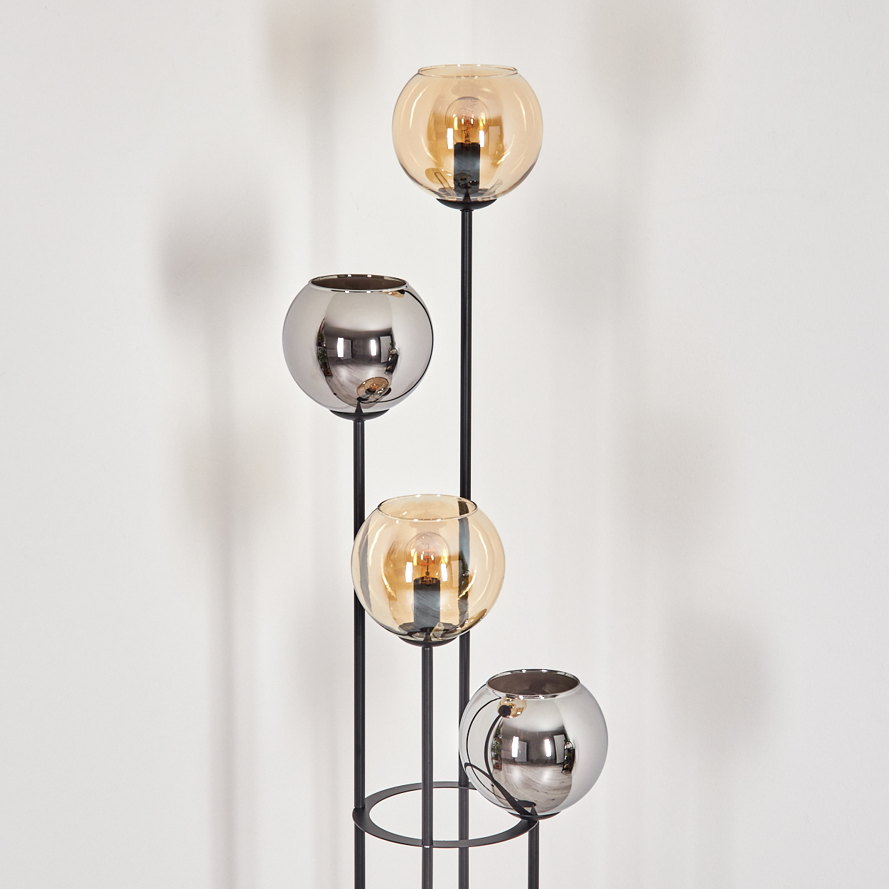 Eine moderne Stehlampe mit vier kugelförmigen Lampen, zwei bernsteinfarbenen und zwei verspiegelten, auf einem schwarzen Metallrahmen.